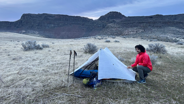 A hiker pulls on a guyline while setting up their tent in Central Washington.