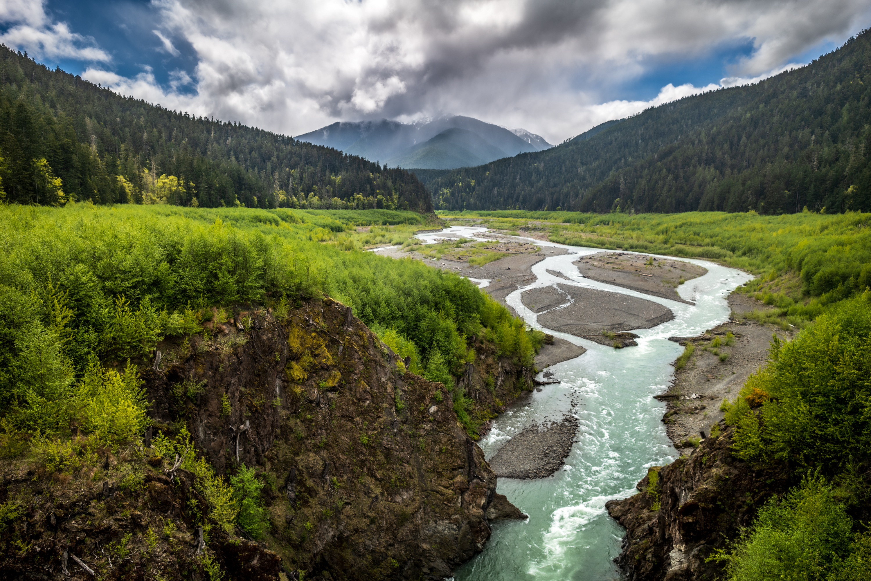 Trailscapes 3rd Place photo by Helge Pedersen Elwah River landscape rushing amongst evergreens and mountains on sunny day.