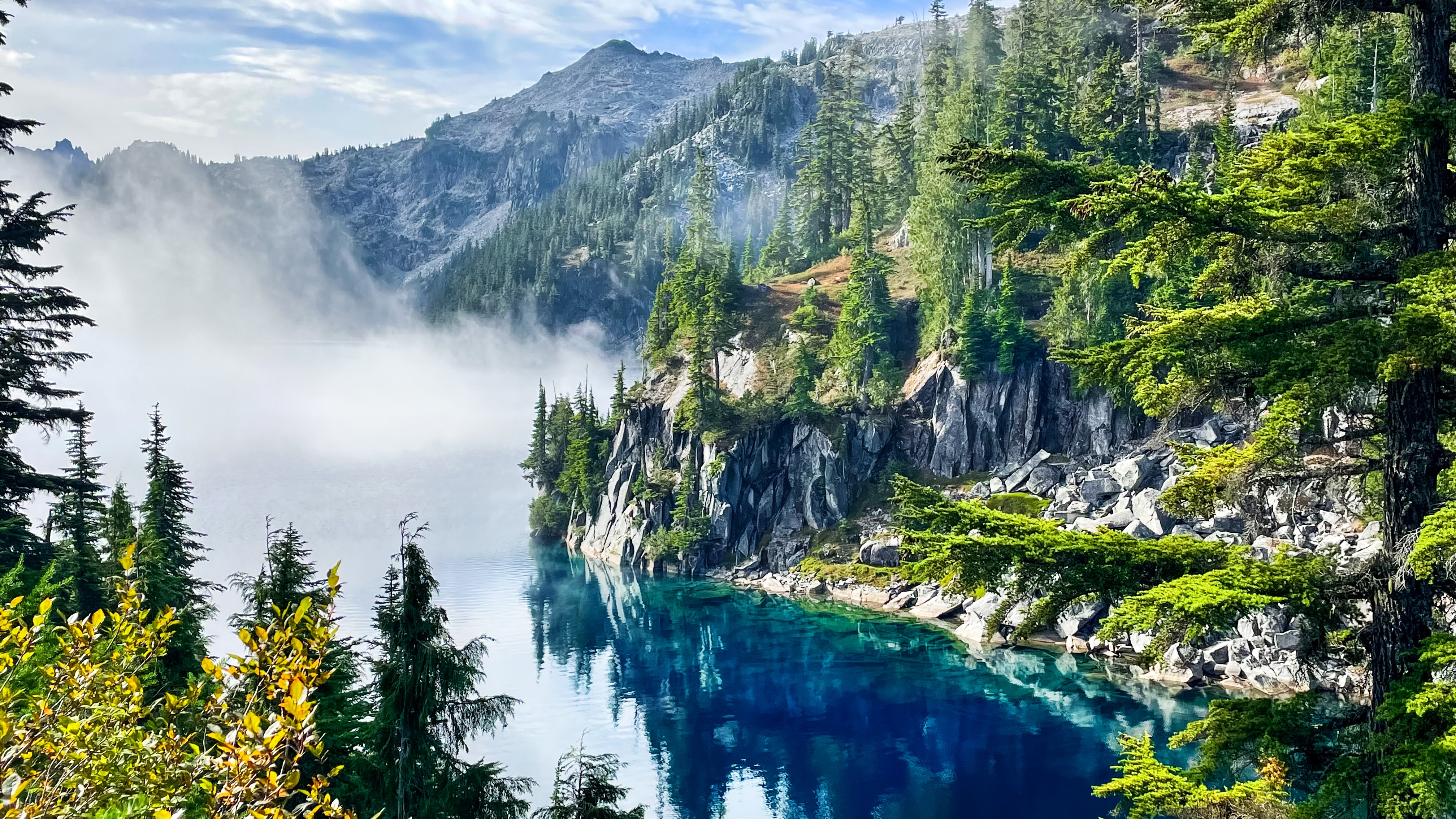 Alpine lake with pine trees and fog framing the lake.