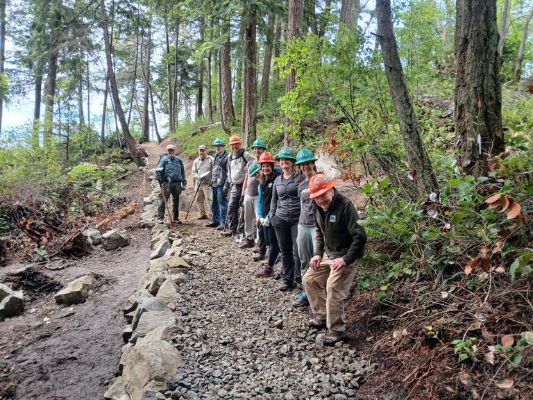 Line of volunteers stand on a newly-finished trail of gravel and with a rock wall to the left. 