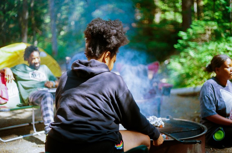 Campers sit around a fire ring in an established campground.