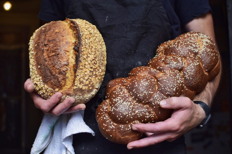 A baker holds a loaf of fresh baked bread in each hand.