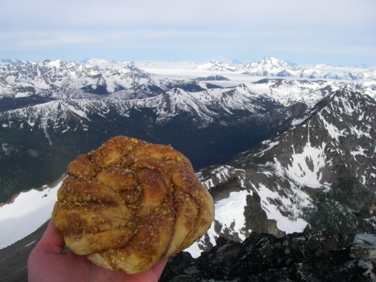 A delicious pastry is held by a hand before a backdrop of snowy mountains.