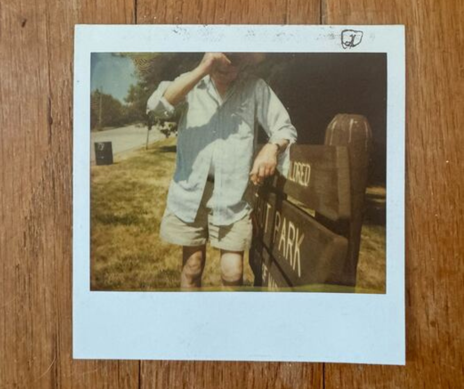 Poloroid by Victoria Obermeyer Photo of Polaroid on wood floor. Man pulls hat over head standing in front of frame.