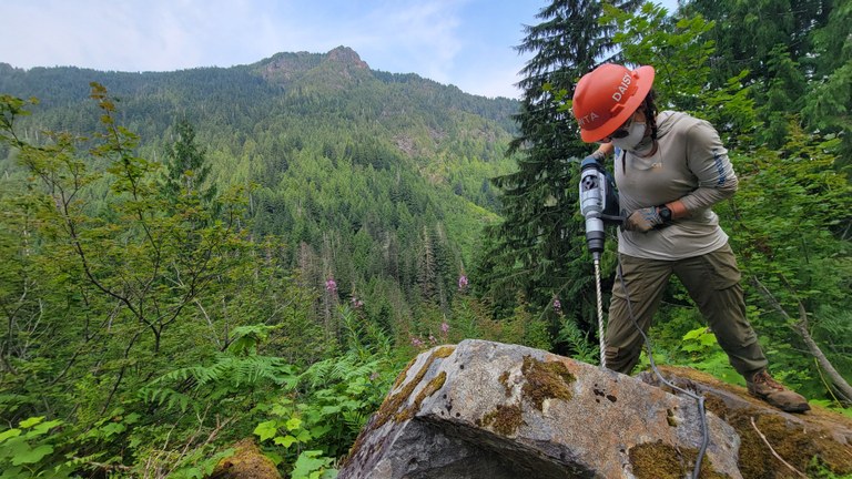 Assistant crew leader Daisy Rios wields a rock drill. This project was made possible with tools and helicopter-drop assistance from Washington Department of Resources. Photo by Joseph Gonzalez A WTA crew member drills through a rock with a rock drill.