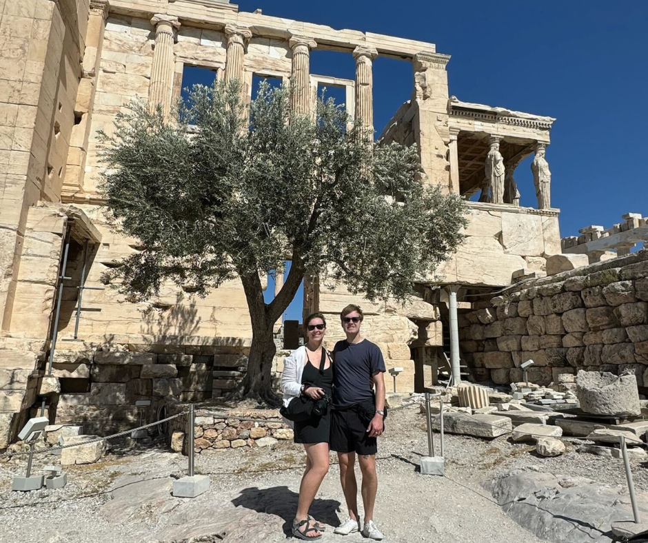 VO in Athens Couple stands in front of olive tree with ancient marble temple in background.