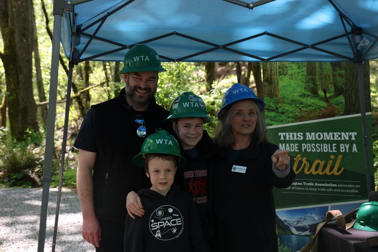 Group of four smiling trail crews under blue tent on trail