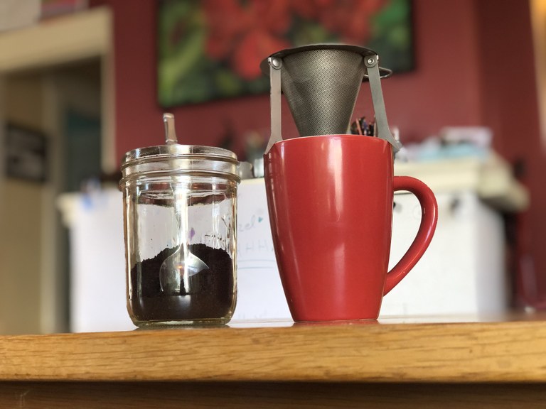 A mug with a small, backpacking drip coffee filter hovering over it. 