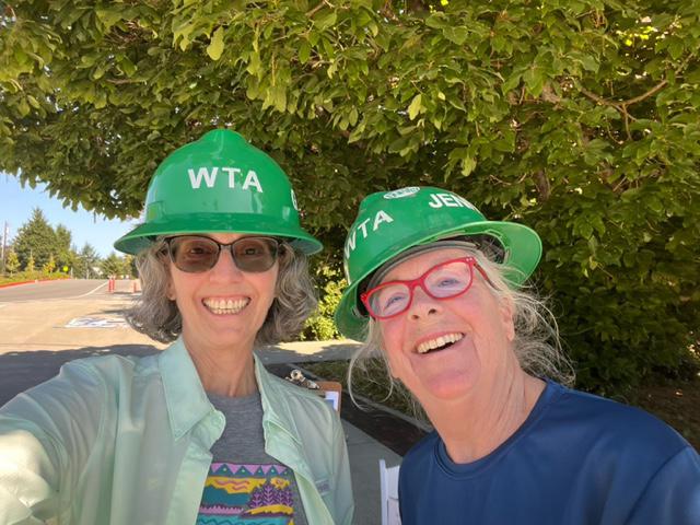 Workshop Leaders Two women pose outside with a tree in the background. They are wearing green WTA heard hats.