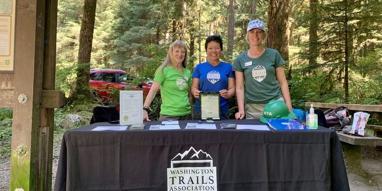 Three WTA ambassadors at a table at a trailhead.
