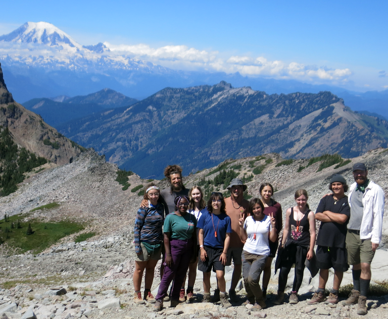 A group of youth and adults pose on trail in front of Mount Rainier. 