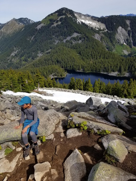 A child sitting on a rock with view of lake and mountain in the background.