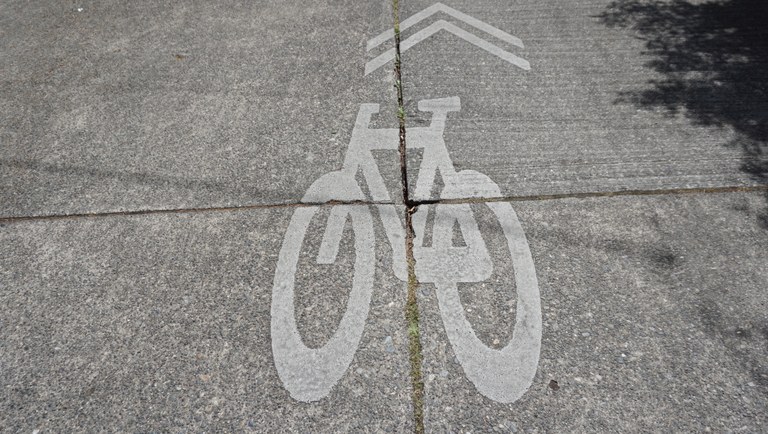 A painting of a bicycle on the street, with arrows pointing forward. 