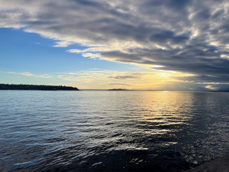 A semi-cloudy sky with an island on the water at sunset. 