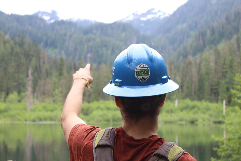 A WTA employee in a blue hard hat points across a lake. 