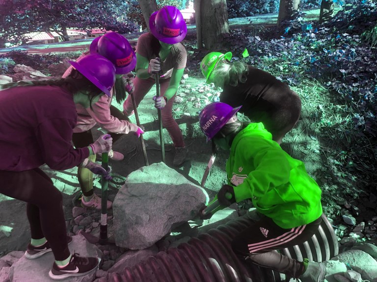 A group of youth volunteer use their combined strength and tools to move a large rock.