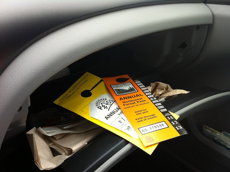 A Discover Pass and NW Forest Pass sit in a glove compartment of a vehicle. 