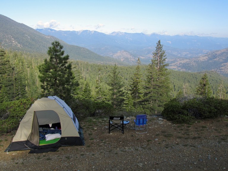 Tent and two camp chairs, with a view of forests and mountain ridges.