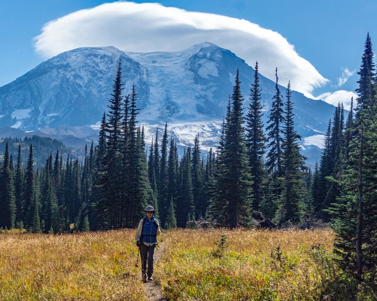 A hiker walks down a trail with Mount Adams rising high in the background. 