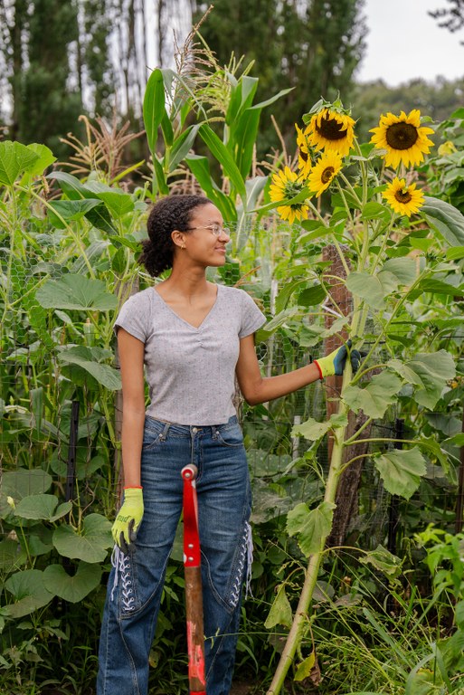 A young women faces a large sunflower plant in a garden.