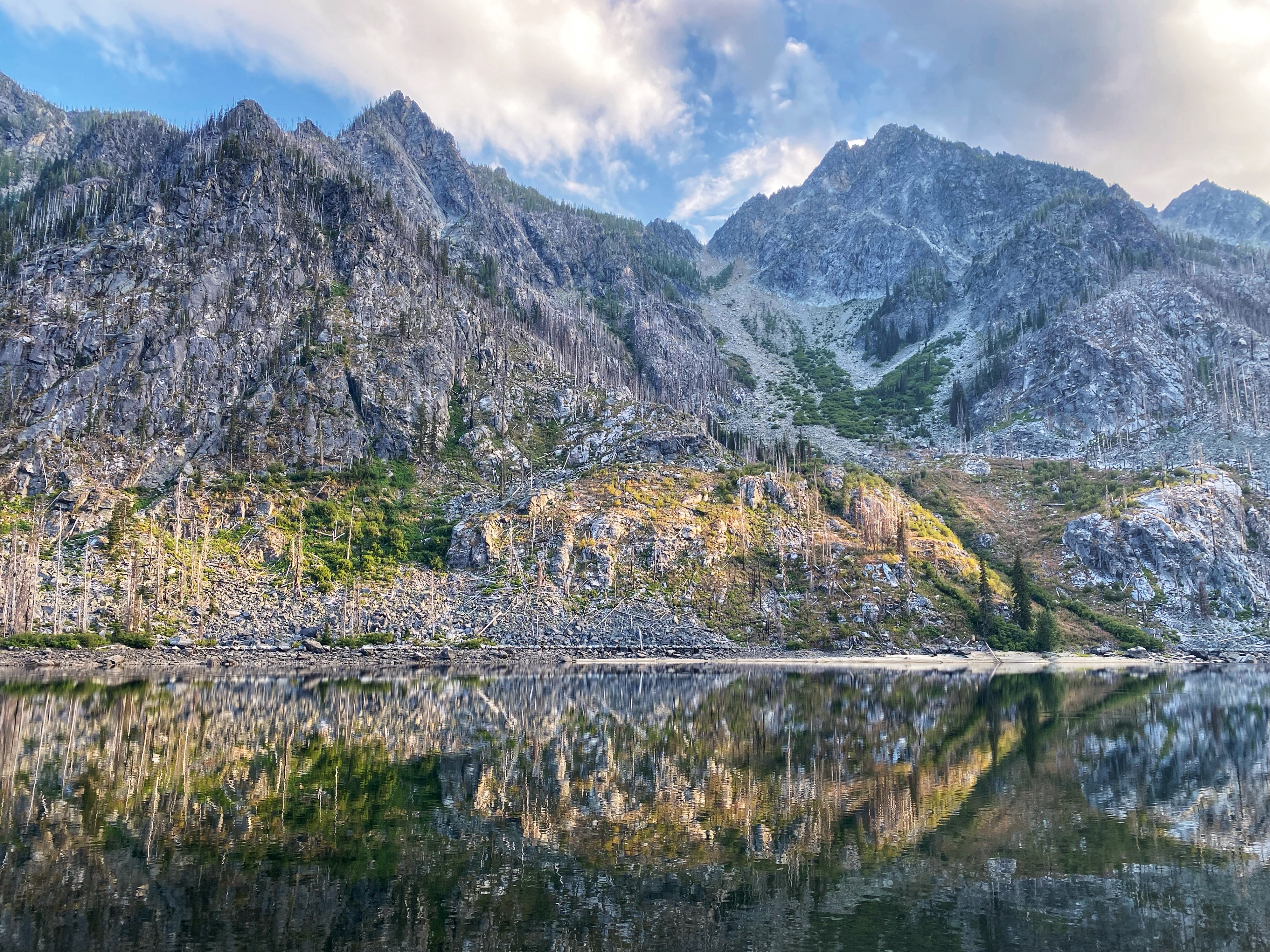 A rocky face with jagged peaks is reflected in the still waters of a lake