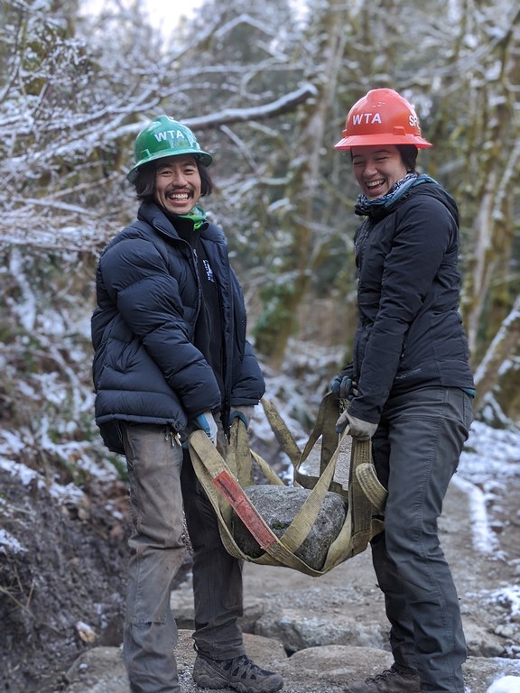 Two people carry a large rock with a rock net.