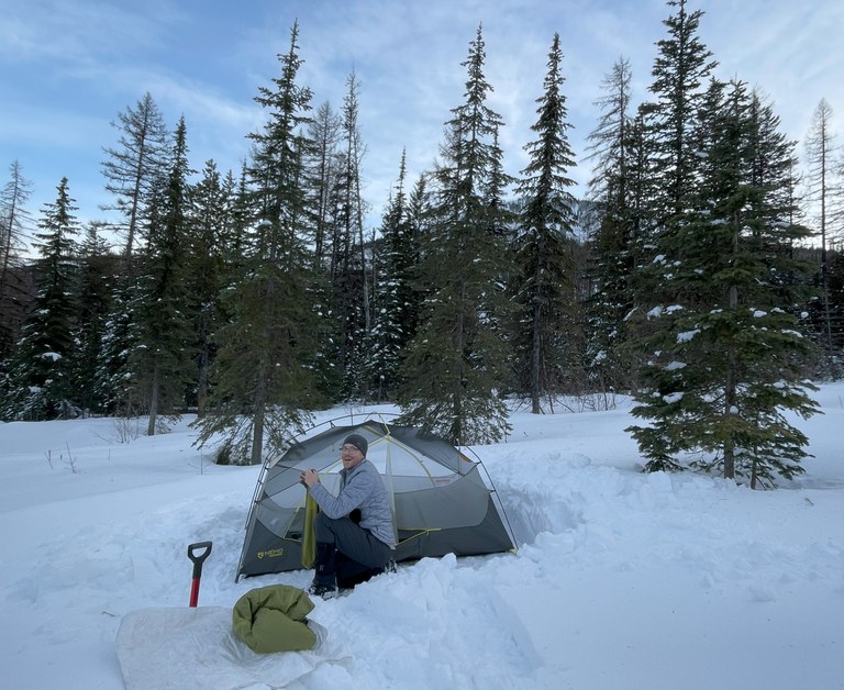 A tent is pitched in a small open meadow under a clear sunset in the winter. 