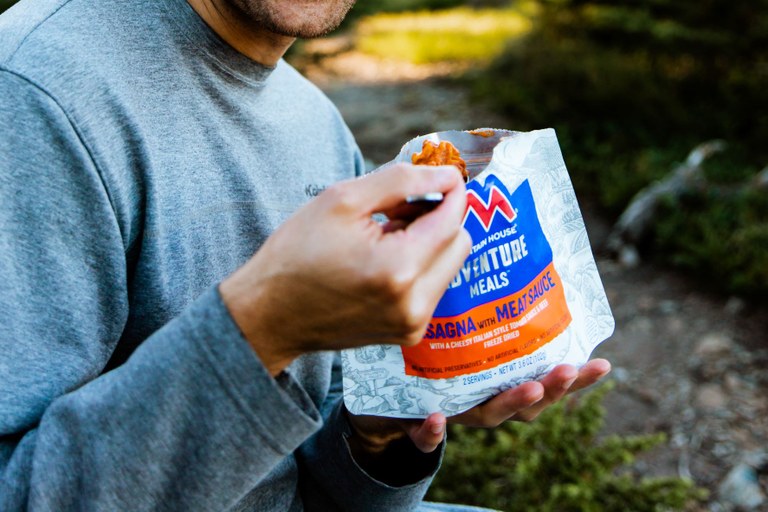 A hiker eats a spoonful of a Mountain Hose meal while on trail.