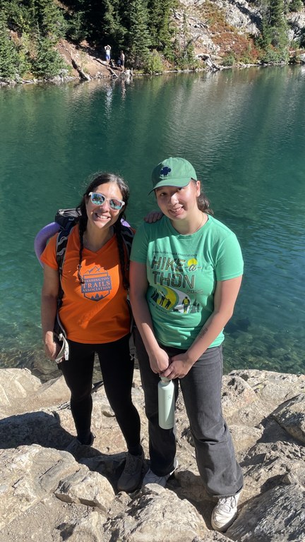 Two hiker stand in front of a blue green lake. 