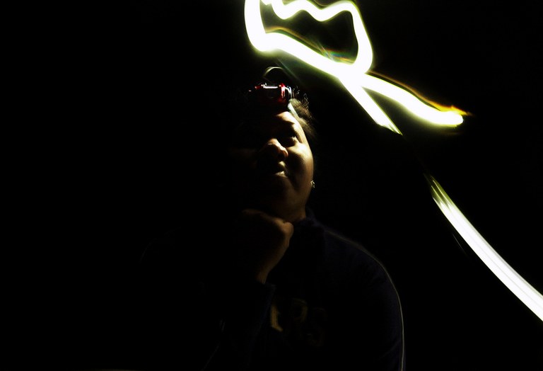 A hiker stands in the night with a headlamp on. They have used the light of the lamp to make a small crown image. 