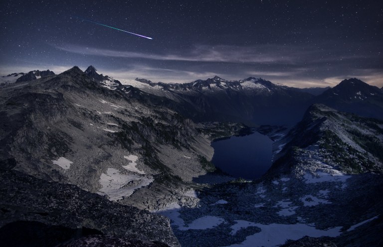 Hidden Lakes A bright shooting star travels across a dark sky above a series of rocky peaks and valleys.