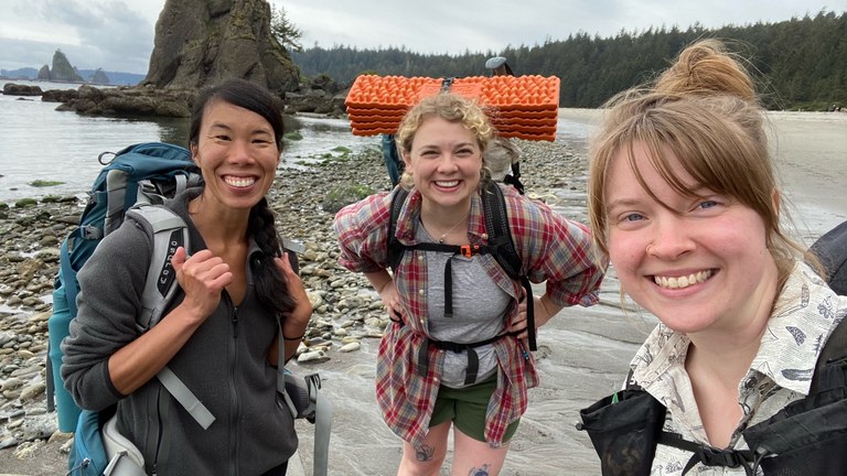 Three friends smile big for a selfie on a beach backpacking trip. 