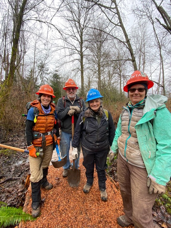 Crew leaders pose together on trail. They're holding shovels and pickaxes on a trail with fresh tread.