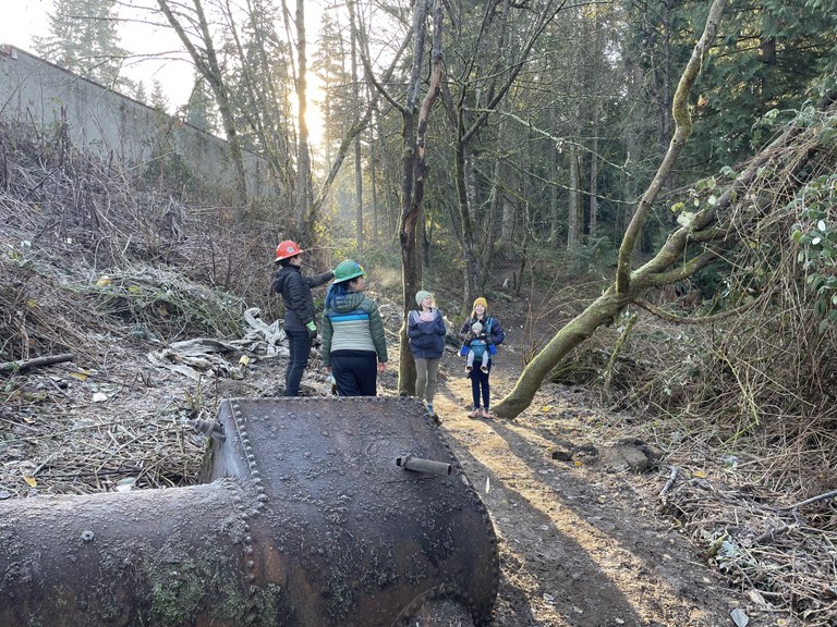 Four people stand on trail next to a large, rusted hunk of metal.