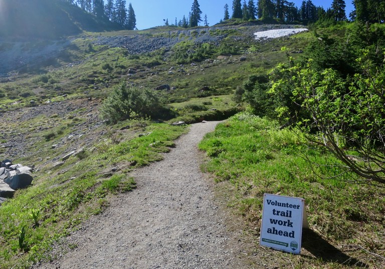 A sign next to a trail reads "Volunteer Trail Work Ahead."