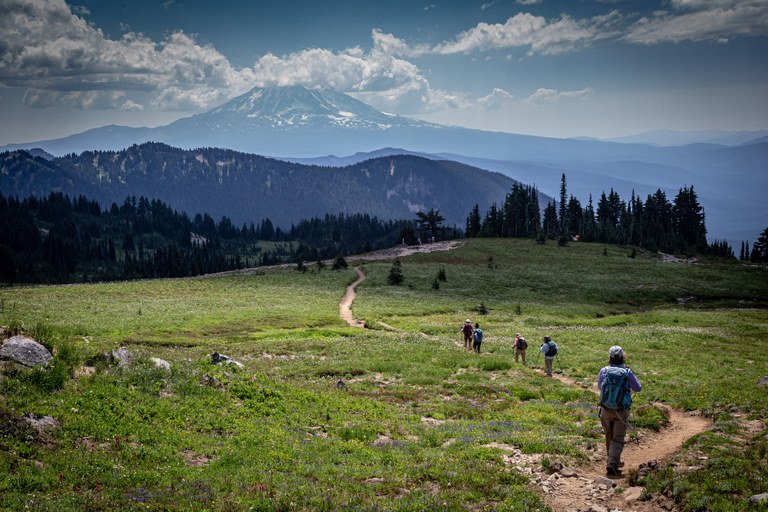 Hikers on the PCT near Goat Rocks. Photo by Don Thompson. Hikers on a clear trail with snow-capped Mt. Rainier in the distance.