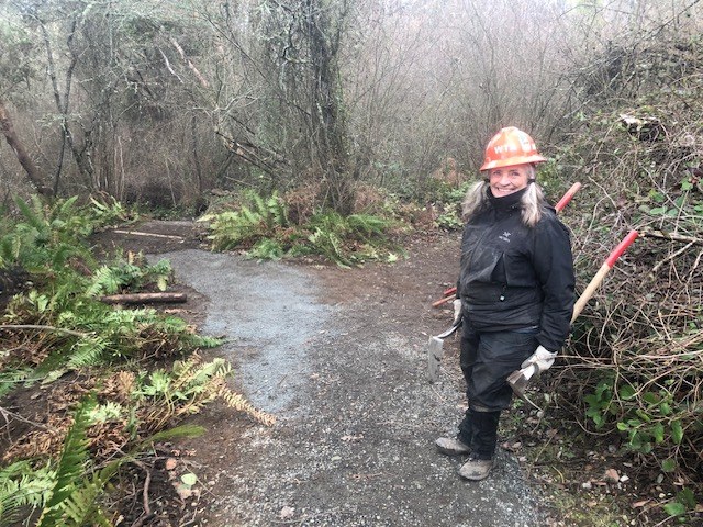 Women in rainjacket holding trail tools with bridge in the background.