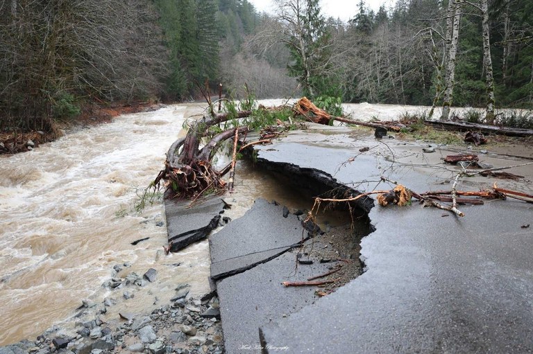 The edges of a paved road crumble into a river. 