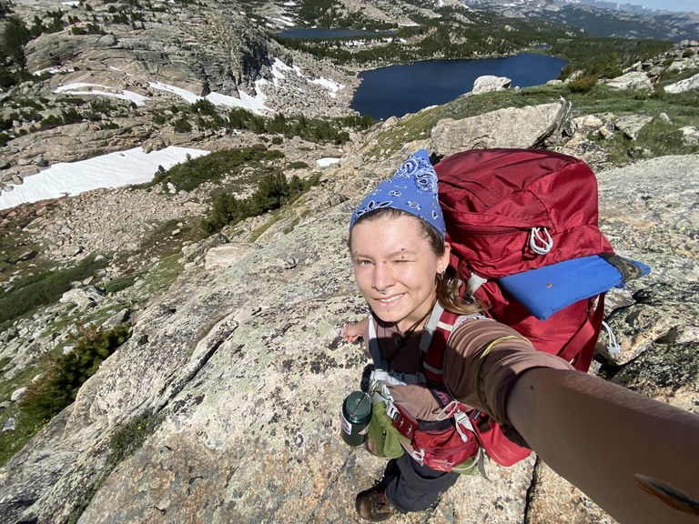 A hiker takes a selfie from atop a huge slab of granite.