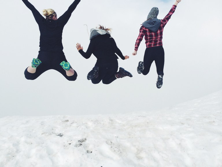 Three hikers jump into the air on a snow-covered mountain. Photo by Veronica Hurm. 