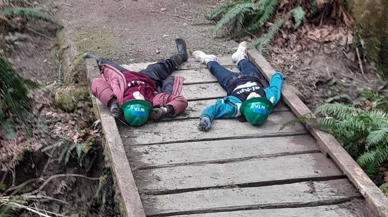 Two youth volunteers lie on a bridge resting Two young people lie on a wooden bridge facing away from the camera.