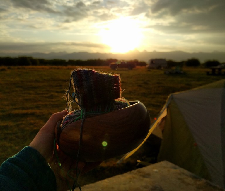 A knitting project held up with a tent in the background.