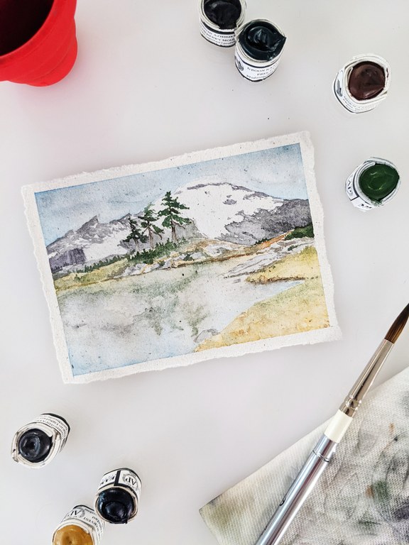 A watercolor image of Mount Baker with watercolor paints visible at the edges.