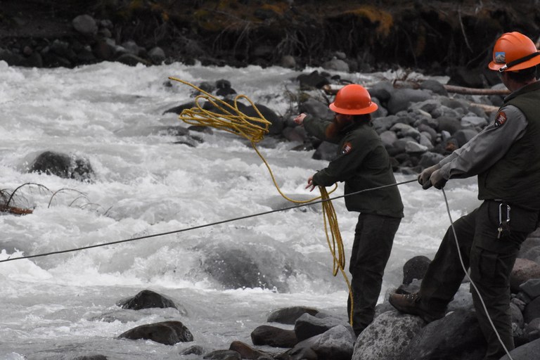 NPS crew members in hard hats use ropes to move the log bridge across the river.