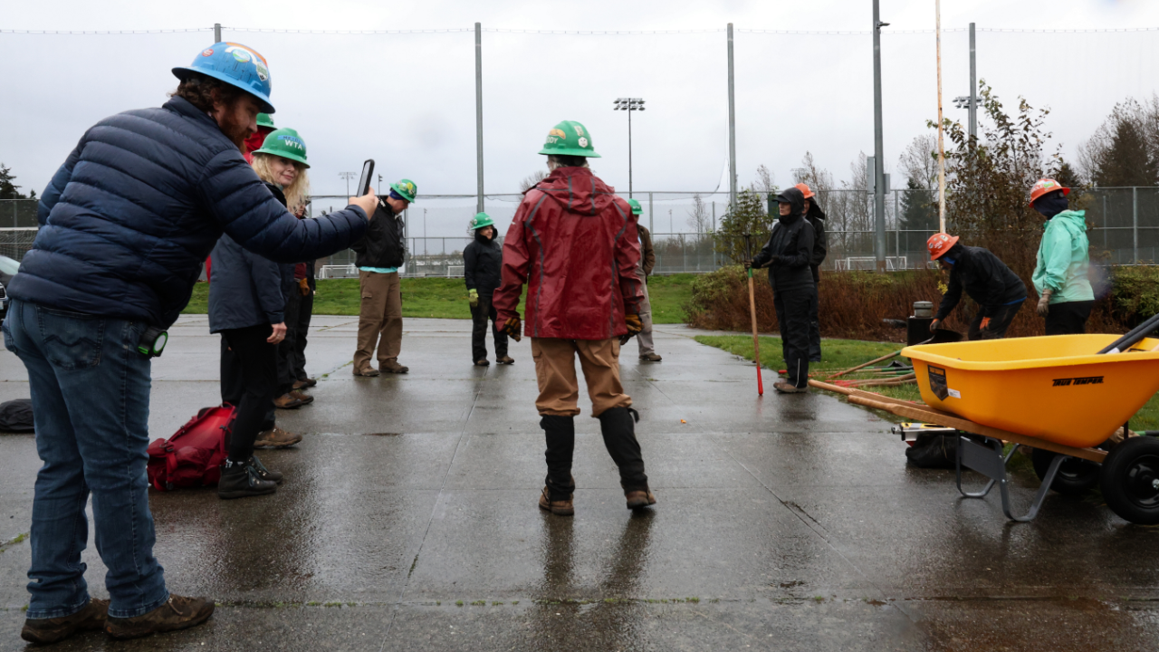 Two images slipt into one. On top you see man in blue flannel talking to crew in a semi circle in a parking lot. The second the same man points his phone at various tools in front of him.