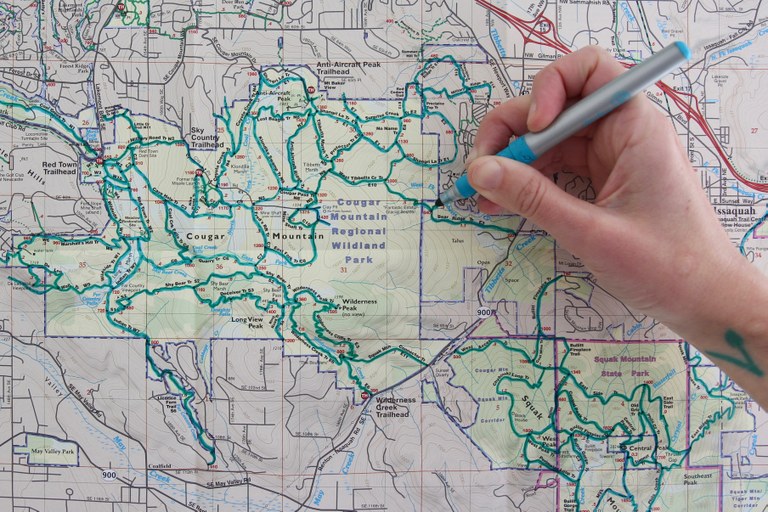 A hand with a colorful marker traces hikes on a paper map.