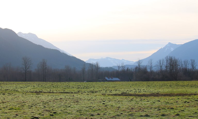 A grassy field and barn in the distance with mountains in the background at Meadowbrook Farm. Photo by trip reporter wafflesnfalafel. 