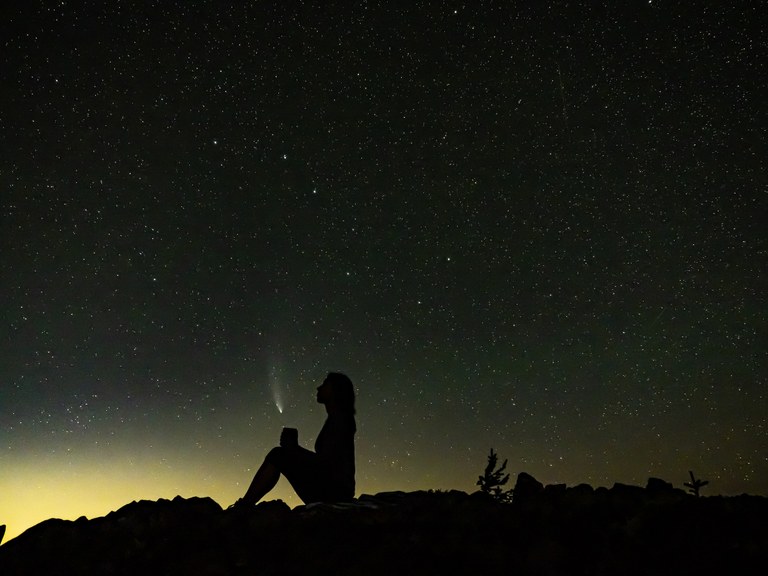 Grand prize winner of the 2021 Northwest Exposure Photo Contest. Photo by Michael Margoshes. Hiker holding cup on mountain with comet at night.