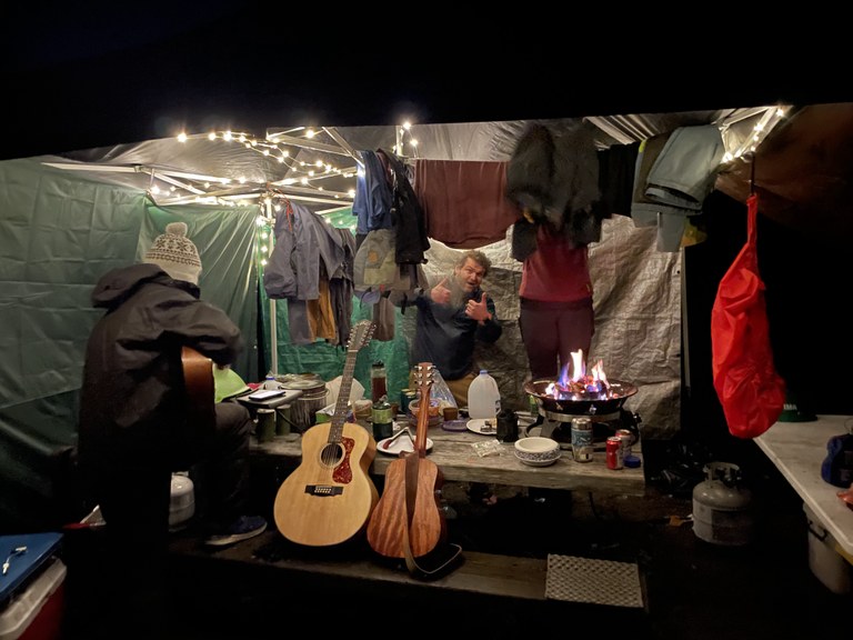 Crew members under a tarp/tent in the rain drying out clothes and other things. Photo by Brandon Tigner.