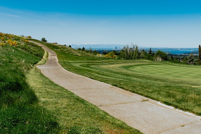 A paved path winding along beside a grass field. 